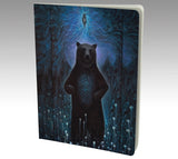 A blank notebook journalwith a painting of a standing bear on the cover, surrounded by a night-time forest setting with a mystical portal above his head and the universe in his belly