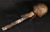 A large handheld rattle with a rawhide head, decorated with a painted sun and moon design and feathers attached to an alder handle.